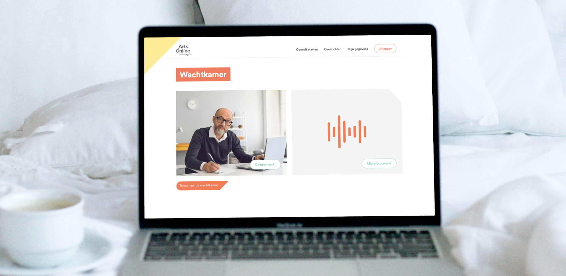 ArtsOnline - Een laptop met de website in een bed met witte lakens en een tas koffie.