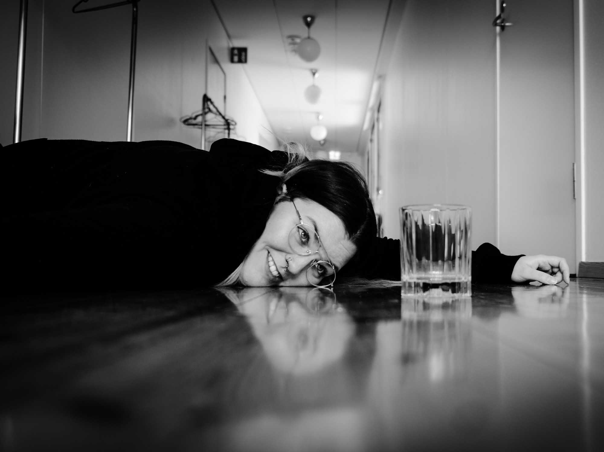Woman laying on floor staring at an empty glass.