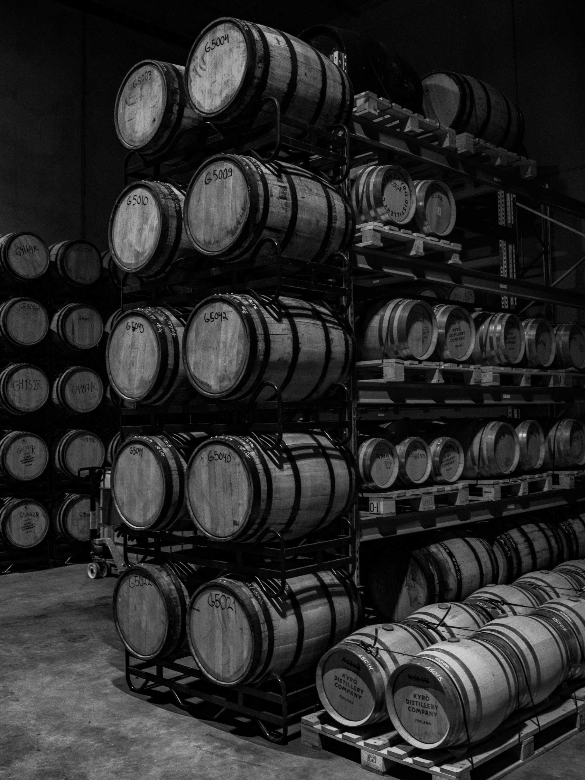 A black and white image of one of the Kyrö barrel warehouses, pictured are wooden barrels stacked atop one another. 