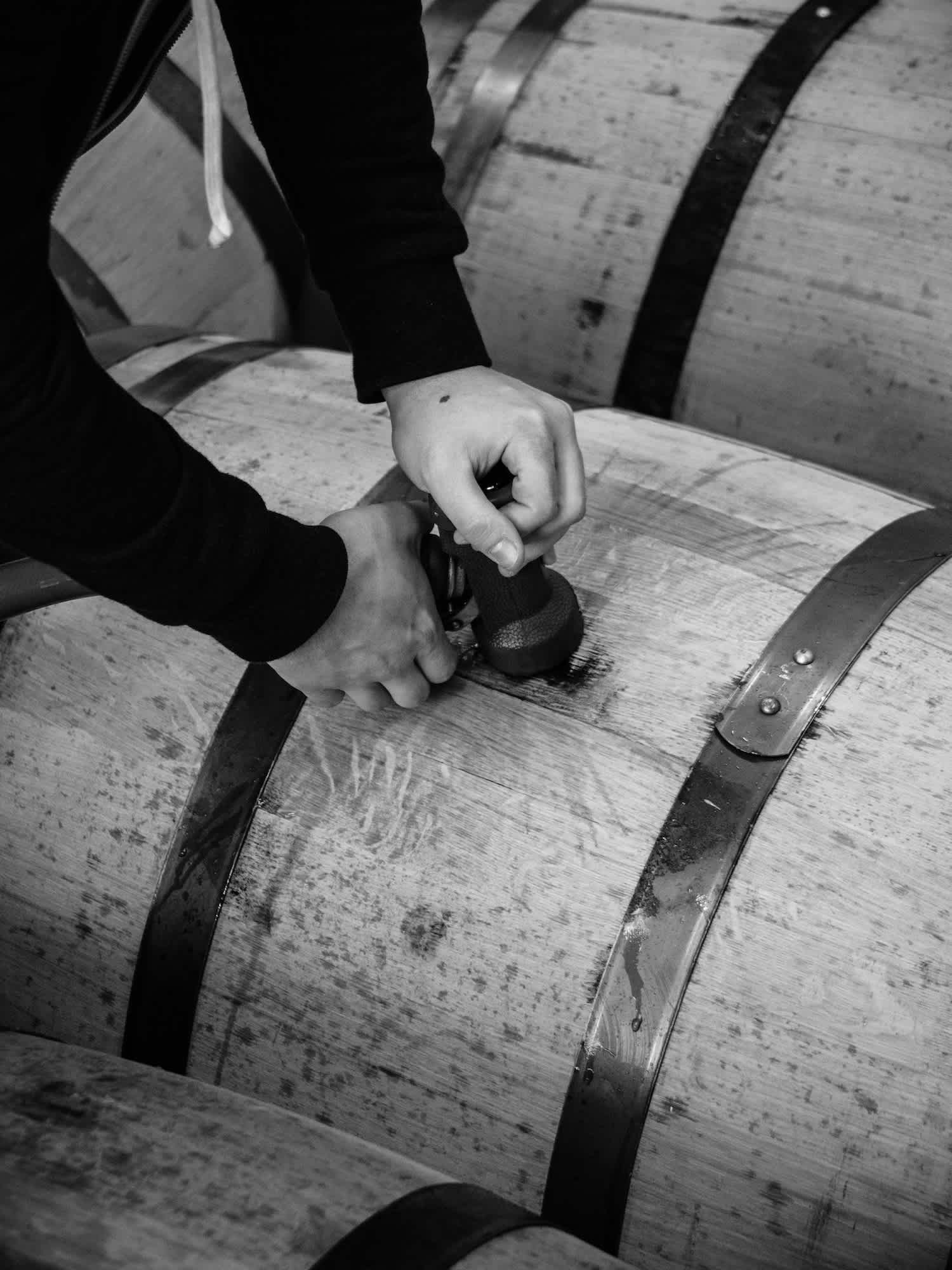 Black and white image of a person filling a barrel with alcohol