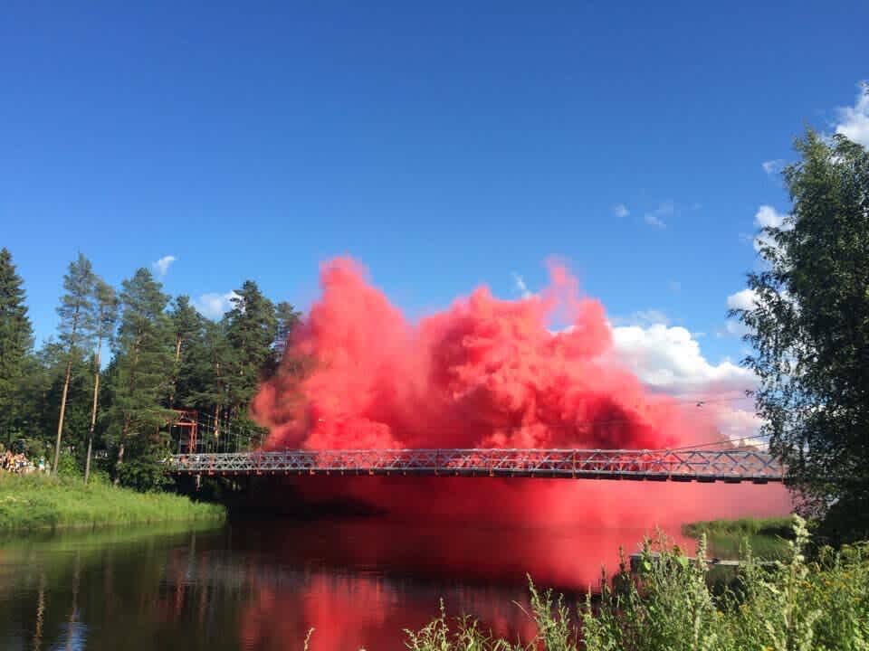 Image of a pink cloud exploding on top of a bridge surrounded by forest and greens. 