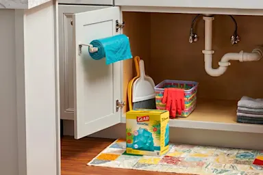 Trash bag roll mounted inside under-sink cabinet beside cleaning supplies and Glad box