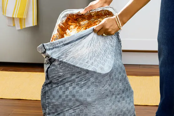 Person in blue pants putting a dirty aluminum pan in a gray trashbag