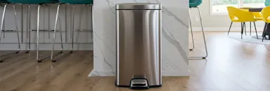 Modern kitchen with stainless steel trash can, marble island, teal bar stools, and yellow chair in background.