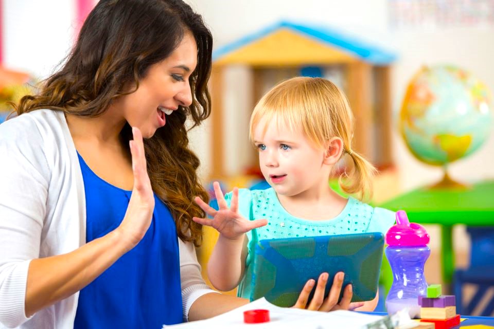 Teacher praises girl on accomplishing a project. The preschooler claps along with the teacher.