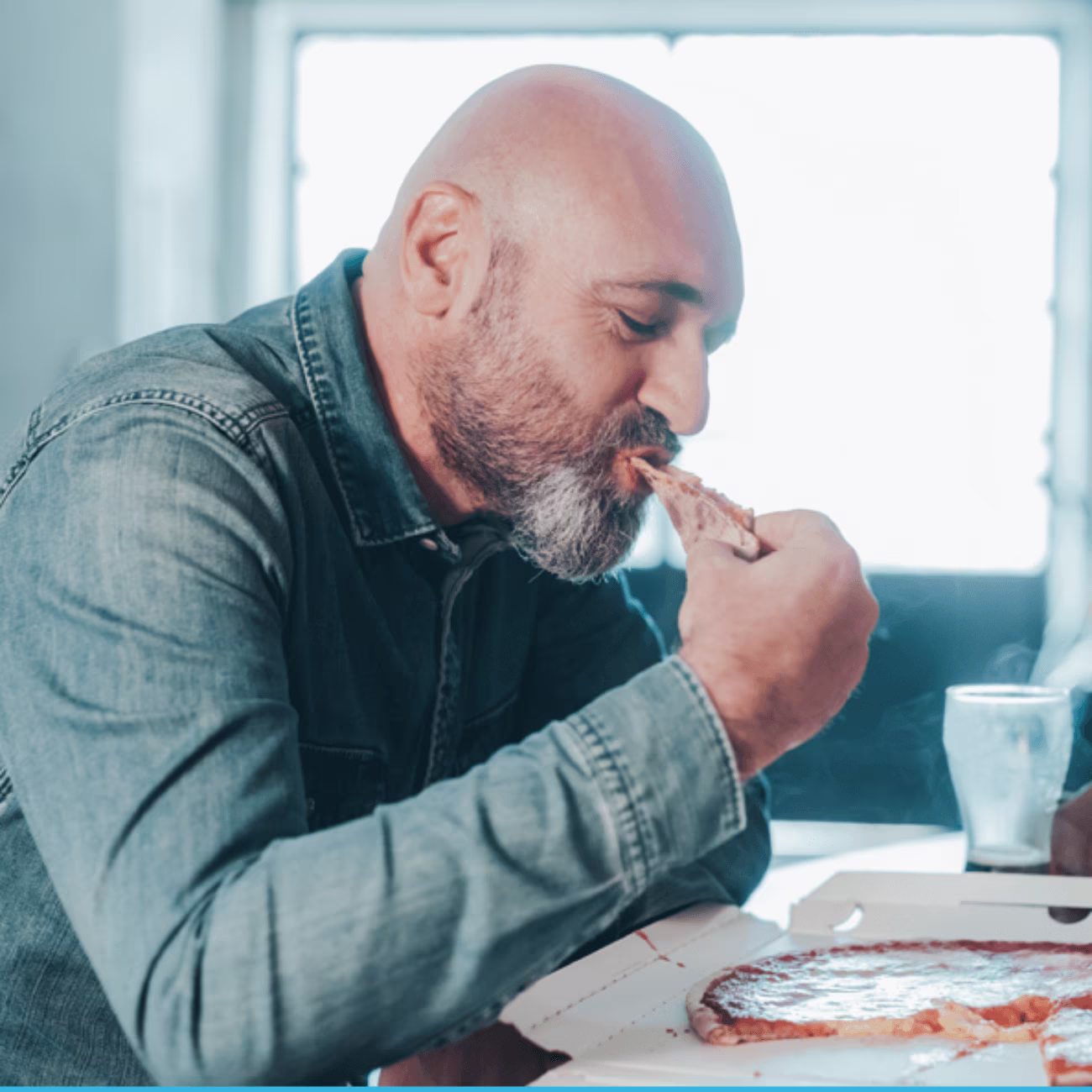 A man with a shaved head eating pizza.