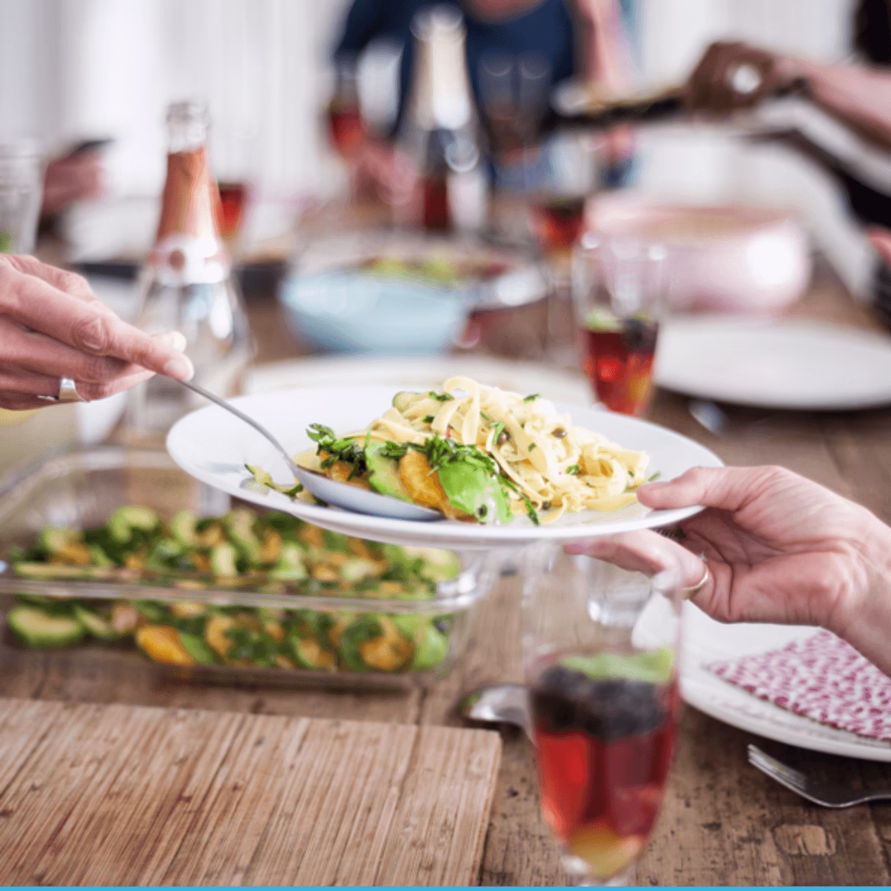 A group of people sharing a meal, with focus on a person serving a salad onto a plate.