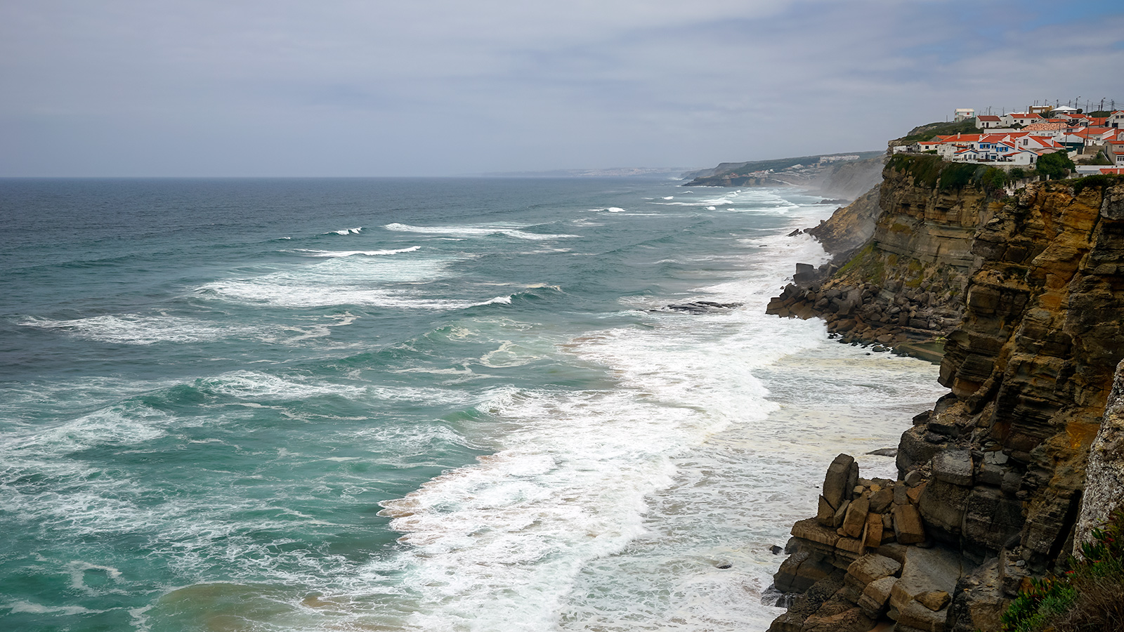 Atlantin aallot iskeytyvät jyrkänteisiin Portugalin länsirannikolla. Kylä jyrkänteellä on Azenhas do Mar.