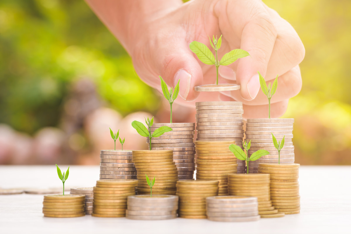 Close up of male hand stacking gold coins with green bokeh background