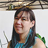 A photo of Steph Mellor. She is smiling and in a co-working space with plants in the background.