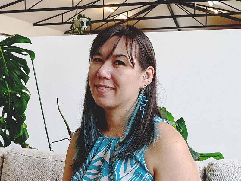 A photo of Steph Mellor. She's smiling and in a co-working space full of plants.