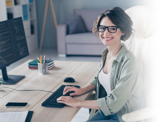 Smiling girl with glasses typing on a computer at a desk