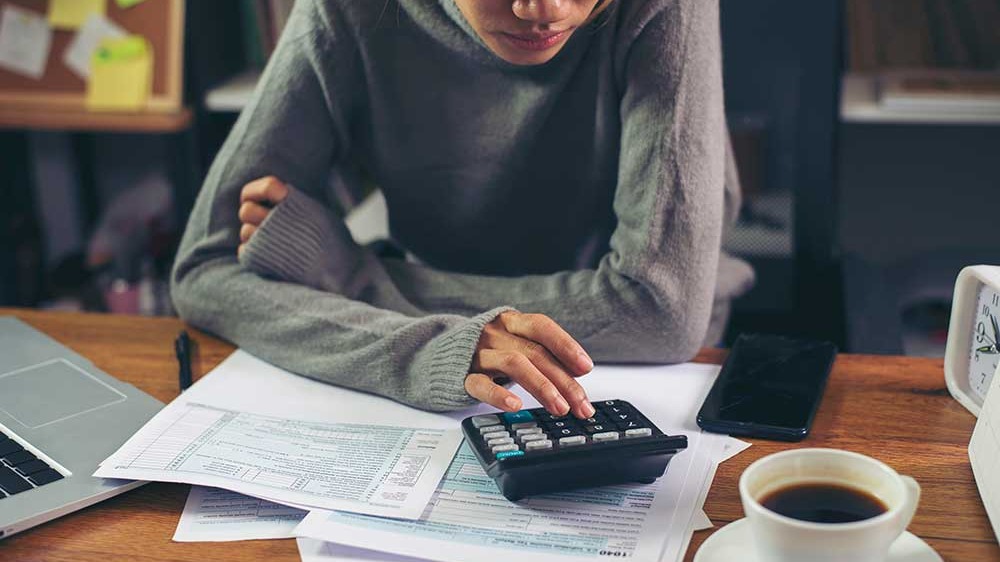 Business woman calculating annual tax on a calculator and using mobile phone.