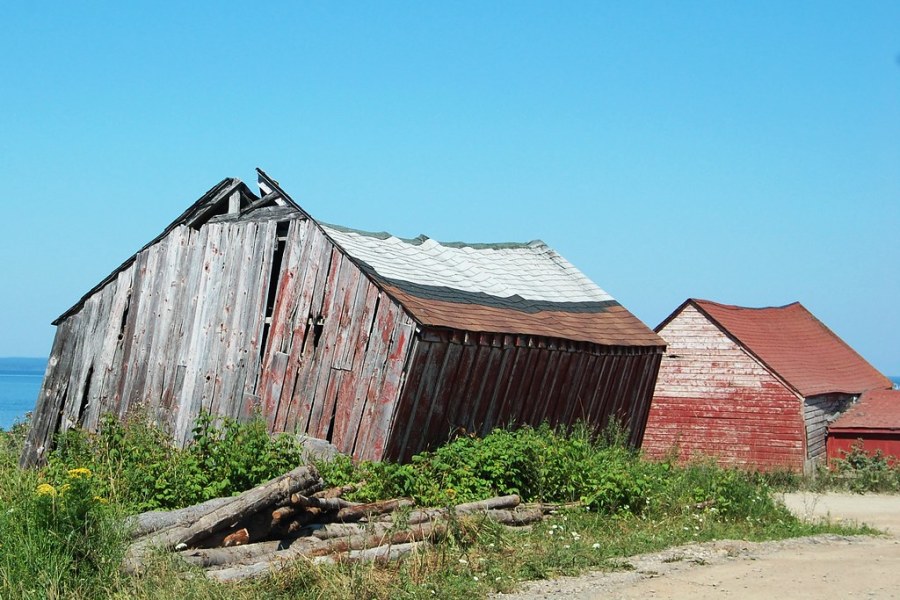 A photo of two small wooden buildings, one of which is dilapidated.
