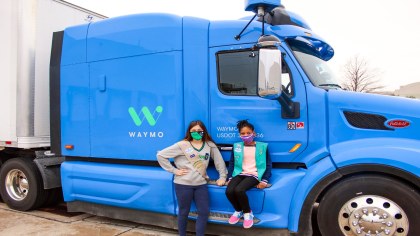 Two girl scouts sit on the cab of a Waymo Via truck 