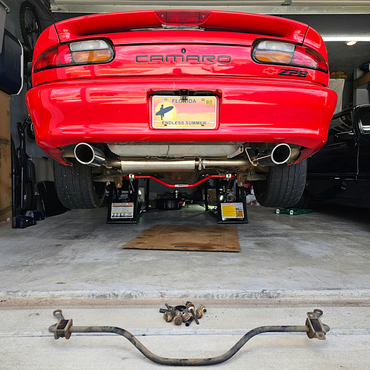 Red Chevrolet Camaro Z28 raised on a QuickJack portable car lift with a removed sway bar on the garage floor.