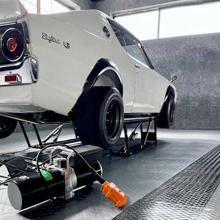 Classic white Nissan Skyline raised on a QuickJack portable car lift with the hydraulic power unit in the foreground.