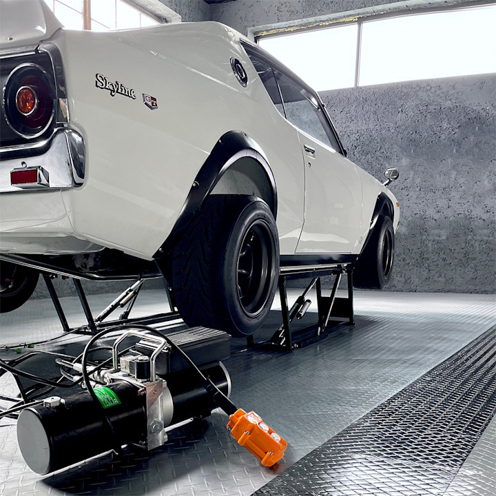 Classic white Nissan Skyline raised on a QuickJack portable car lift with the hydraulic power unit in the foreground.