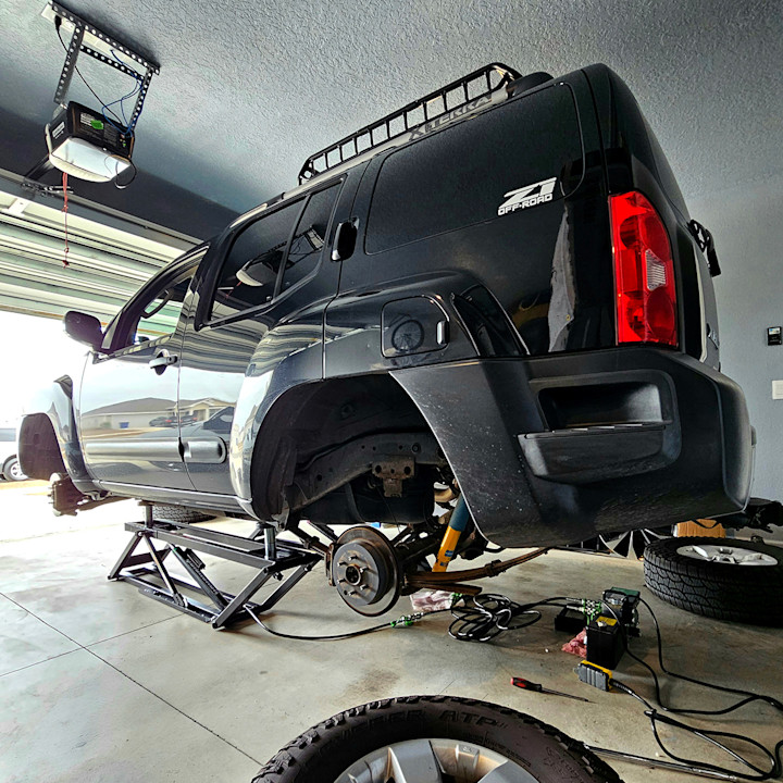 Rear view of a Nissan Xterra raised on a QuickJack portable car lift with its wheels removed in a home garage.