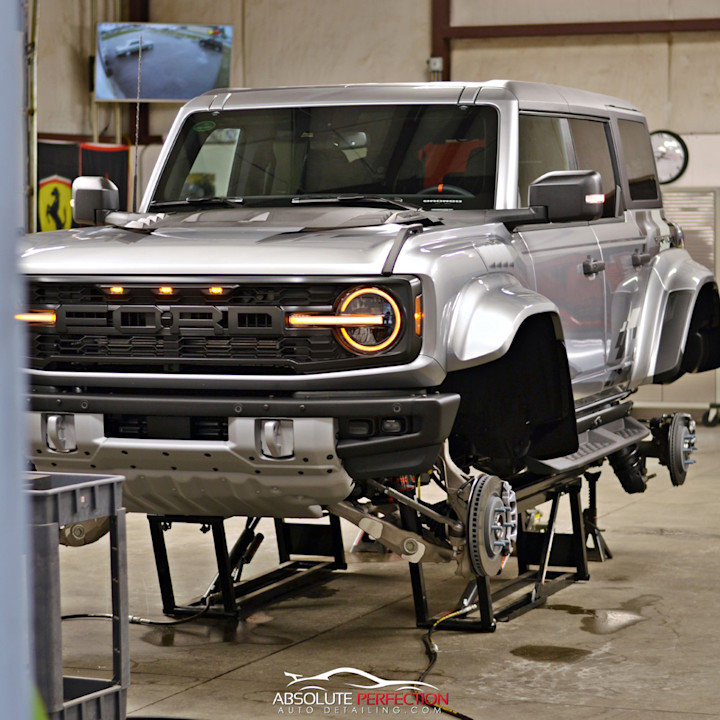 Silver Ford Bronco raised on a QuickJack portable car lift with its wheels removed in a workshop.