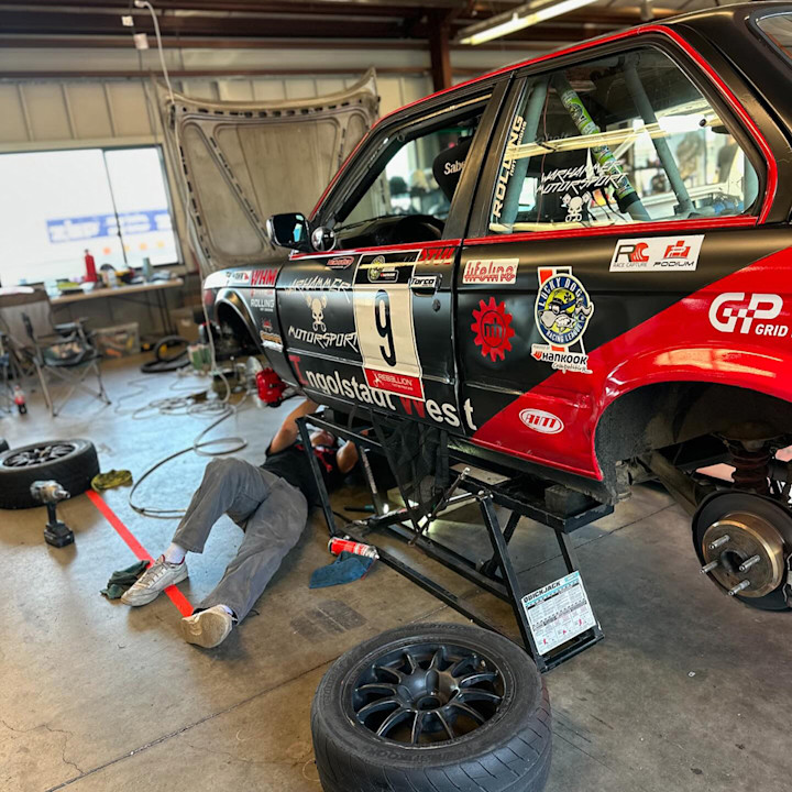 Mechanic working beneath a race car raised on a QuickJack portable car lift with its wheels removed.