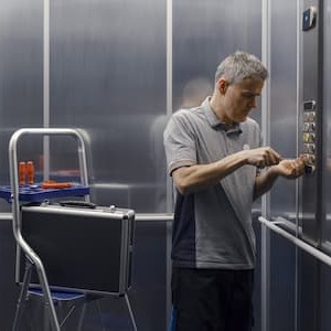 Maintenance technician repairing an elevator control panel with a screwdriver.