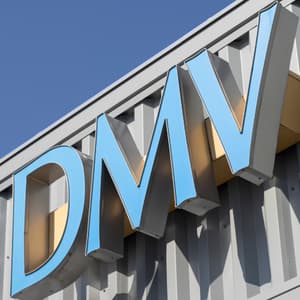 A large blue DMV logo is mounted on the white exterior facade of a modern commercial building under a clear blue sky.