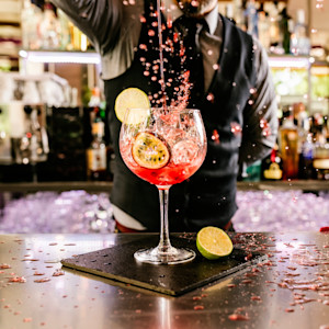 Male bartender in Texas pours a red cocktail beverage into a large wine glass with citrus garnishes.