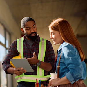 A Black male contractor looks over plans with a white female carpenter.
