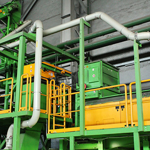 A large piece of industrial processing equipment is shown inside a manufacturing facility, featuring a green metal structural frame and bright yellow safety guardrails.