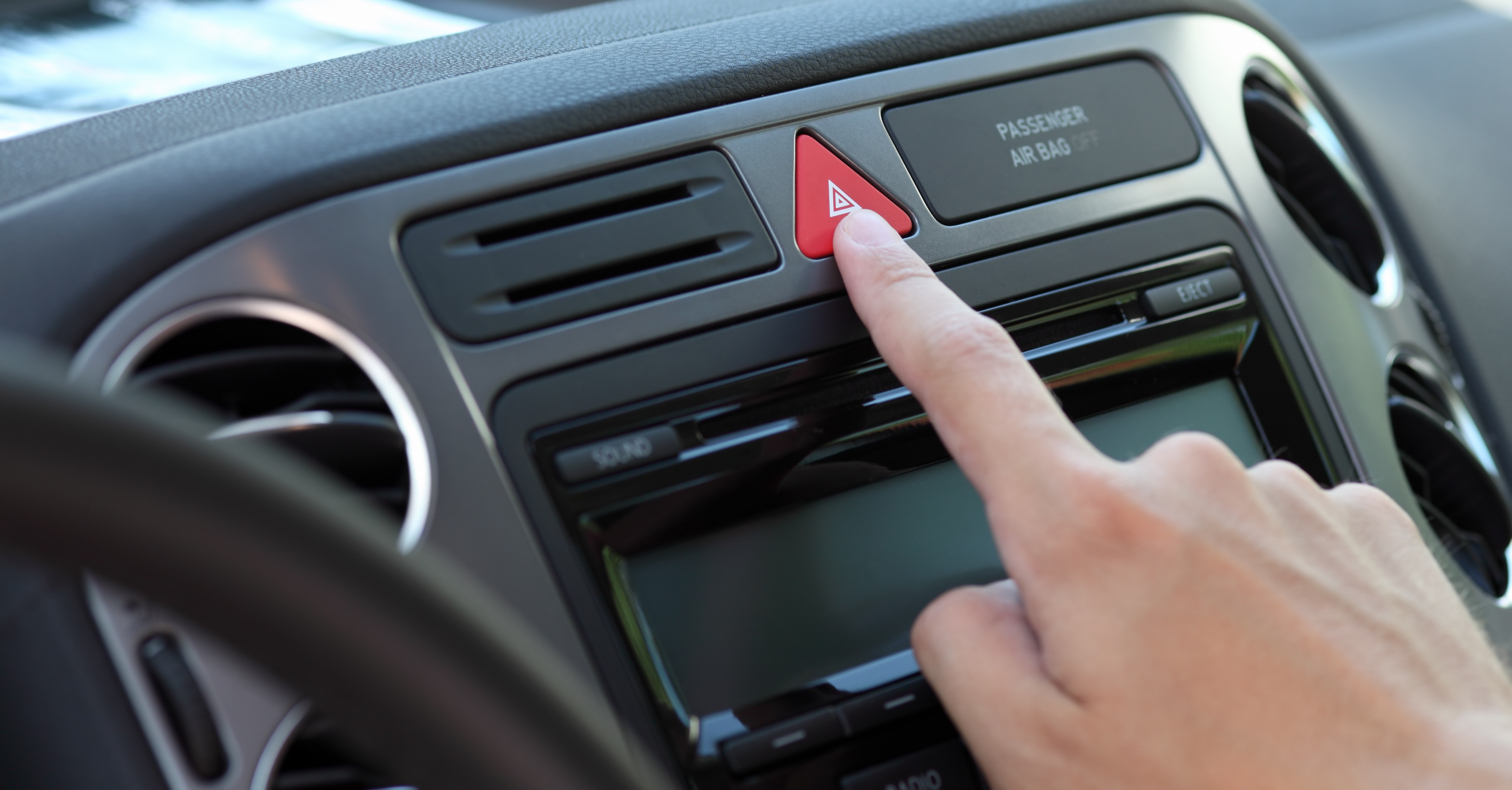 Image of someone pushing the hazard lights button on their car.