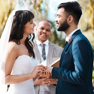 A young bride wearing a wedding dress exchanges vows with a young groom wearing a suit while a man behind them officiates.