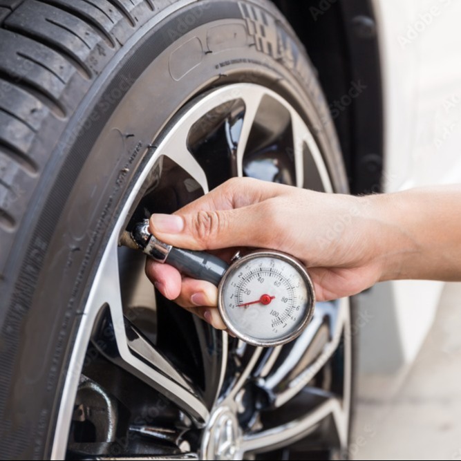 A person checking a vehicle's tire pressure with a tire gauge.