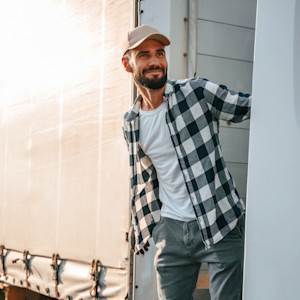 A smiling man stands between a semi cab and trailer during sunrise.