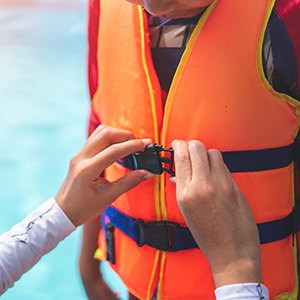 A close-up shows someone securing the buckle on an orange life jacket.