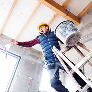 A construction worker wearing a yellow hard hat and blue vest loses balance on a wooden ladder while carrying a bucket.