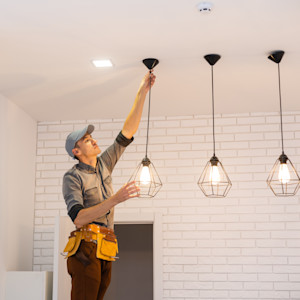 A male electrician installs pendant lights in a home.