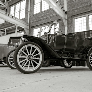 A classic early 20th-century automobile with large spoked wheels and an open-top design is displayed inside a historic brick building.