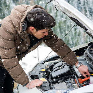 A man looks under the hood of his car during a snow storm.