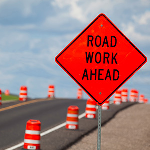 Orange road work ahead sign on the side of the road.