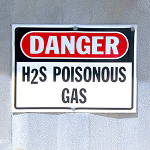 A safety sign on an industrial wall warns workers about the presence of poisonous hydrogen sulfide gas.