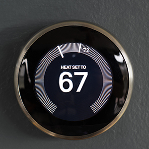 A round digital smart thermostat mounted on a wall shows that the heat is set to 67 degrees.