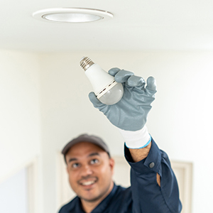 Worker replacing a recessed ceiling light bulb.