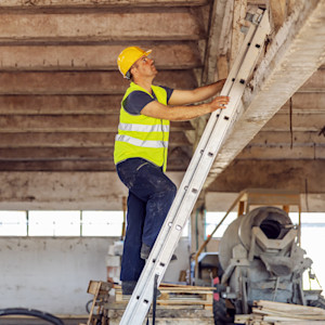 A construction worker climbs an extension ladder to work in the rafters of a warehouse.