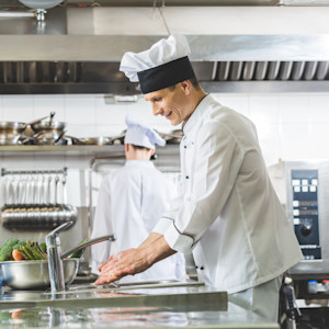A professional chef in a commercial kitchen washes his hands in a handwashing sink.