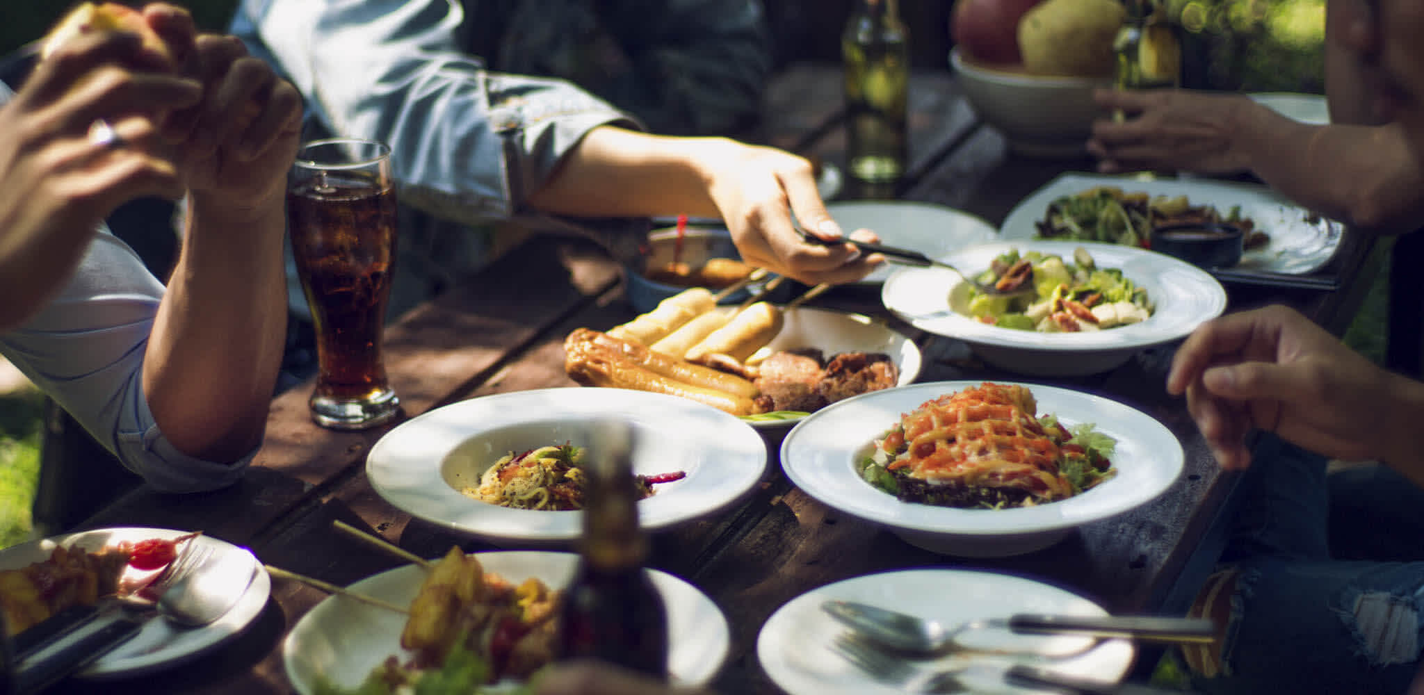 Pessoas se servem em mesa de madeira repleta de refeições saudáveis