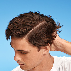 Nahaufnahme eines Mannes mit gescheiteltem braunem Haar, der seinen Nacken berührt.