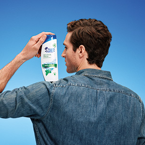 Mann hält eine Flasche Head & Shoulders Menthol Fresh Shampoo über seiner Schulter.