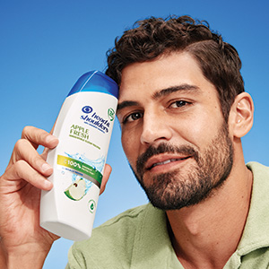 Mann hält eine Flasche Head & Shoulders Apple Fresh Shampoo neben seinem Gesicht.