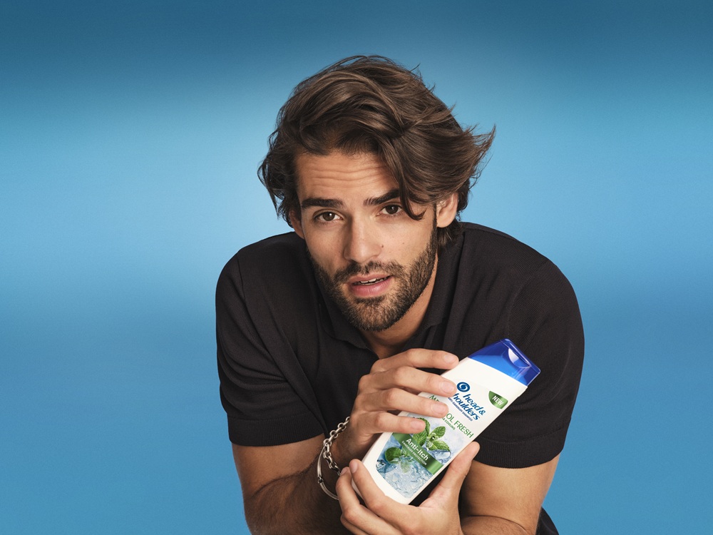 Ein gutaussehender Mann hält eine Flasche Head&Shoulders Menthol Fresh Shampoo in den Händen.